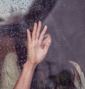 Young woman with panic looking distraught on the inside of a window with rain drops